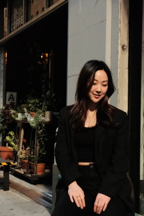 Lena Yeo, founder of LEMI Office, seated outside a New York storefront in the sun